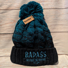 Load image into Gallery viewer, Teal and black knit Badass beanie with pom-pom on a wooden surface