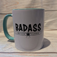 Load image into Gallery viewer, White mug with teal handle featuring the word 'BADASS' on a wooden surface