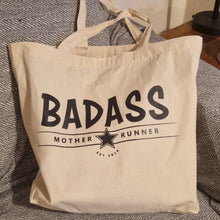 Load image into Gallery viewer, Beige tote bag with 'BADASS MOTHER RUNNER' text on a textured surface
