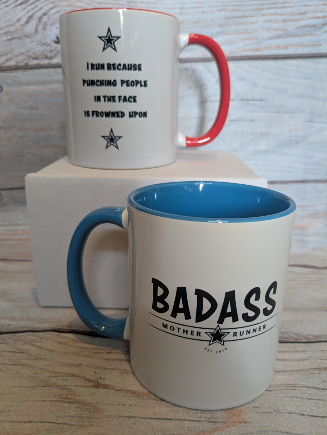 Two mugs in red and blue with humorous text designs on a wooden surface