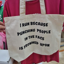 Load image into Gallery viewer, beige tote bag with i run because punching people in the face is frowned upon in black text
